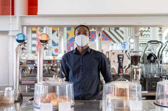 a member of staff wears a mask and stands behind the bar in the cafe