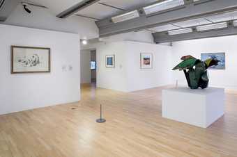 installation view showing a sculpture in the middle of a gallery space and artworks on the wall