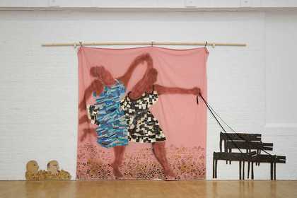 A large installation made of three main parts: two cut out paintings of heads on the floor, a large pink bedsheet with a painting of two Black women holding hands and dancing or running, and cut out paintings of four dogs that are attached to the larger p