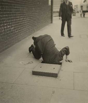 man looking into a sidewalk vent on a London street.