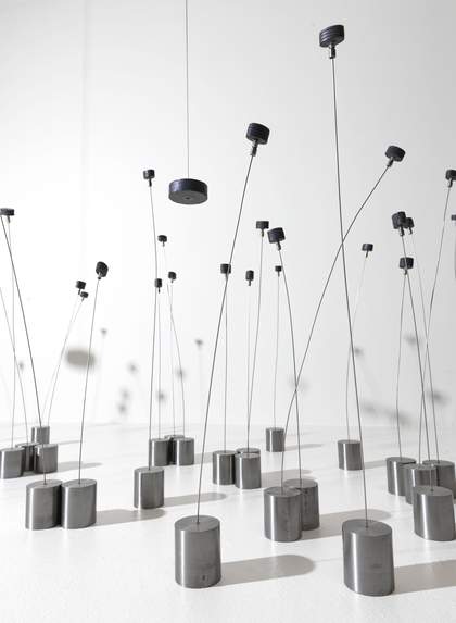 A close-up, worm's eye view of a handful of circular silver-coloured metal magnets attached to thin, long silver strands against a white background