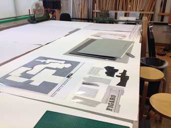 A paper collage replicating the original Picasso under construction on a work table surrounded by paper and a cutting blade