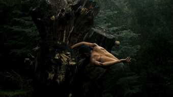 a topless man dances in a forest
