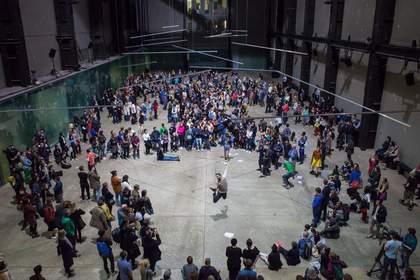 Male dancer leaping whilst being watched by a crowd which circles around him
