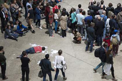 Image of a crowd watching solo dancers lay on the floor surrounded by paper in the Turbine Hall
