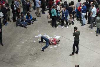Close up of male dancer on the floor in the Turbine Hall surrounded by torn paper, a crowd is watching