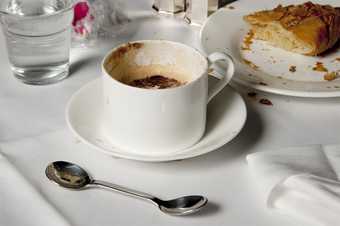 photograph of coffee, double ended spoon and cake on a white tablecloth