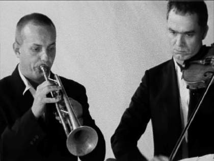 Two men in suits play intruments, one the violin, the other the trumper