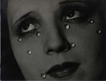 A black and white photographic portrait of a close up of a woman's face with glass tear drops at various places on her face