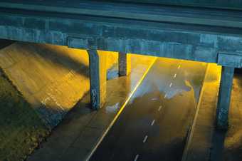 A blue and yellow photograph of the underside of a motorway flyover. The underpass is graffitied and illuminated by sodium yellow lamps