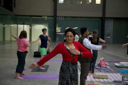 A meditation class in Turbine Hall with people standing on yoga mats