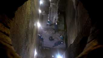 five figures wearing dark boiler suits are seen from above, in what looks like an underground tunnel. the photo is framed by a round brick opening.