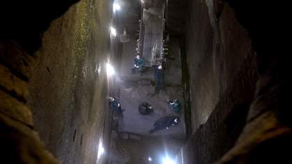 five figures wearing dark boiler suits are seen from above, in what looks like an underground tunnel. the photo is framed by a round brick opening.