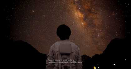 The back of a person in a space suit looking up at a dark but starry sky.