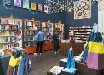A shop with dark blue walls full of books, postcards, prints and tote bags