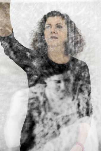 Photograph of the artist with her arm raised with a projected image of a female portrait on her