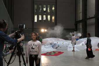A girl stands infront of a camera in Tate's Turbine Hall 