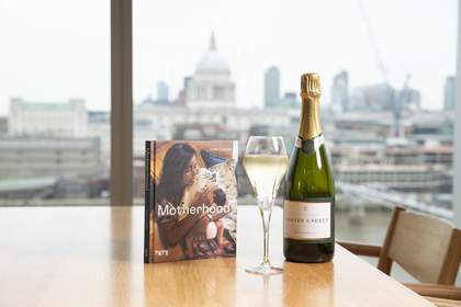 A book called 'motherhood' is stood up on a table next to a bottle of champagne
