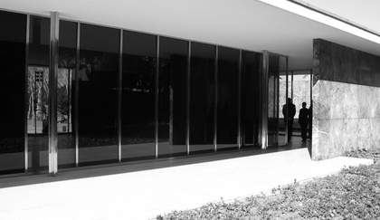 two people seen entering a glass and concrete building in the distance