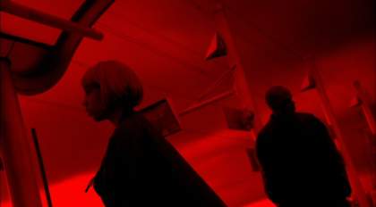 Two people standing in a room lit by red light.