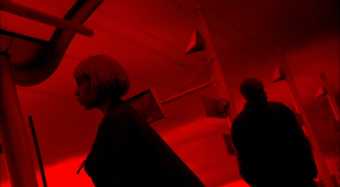 Two people standing in a room lit by red light.