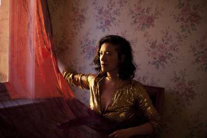 Photograph shows a woman in an interior looking out of a window