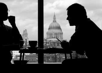 Black and white photograph of two Tate Members in coversation in the Members room with view of St Pauls behind them