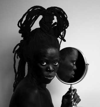 Black and white photo of the artist holding a mirror