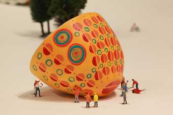 photograph of a brightly coloured and patterned ceramic jelly mould on its side surrounded by small figures