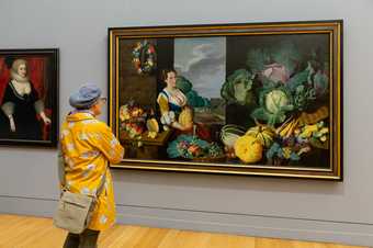 A person looks at a large painting featuring a woman and many vegetables