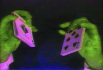 two fluorescent green hands holding fluorescent pink playing cards.