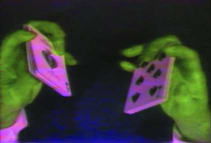 two fluorescent green hands holding fluorescent pink playing cards.