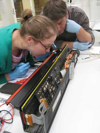 Two conservators examining a black box of electronics
