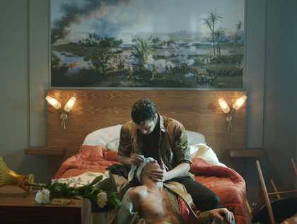 a man sits and holds the head of a man who has a blindfold on