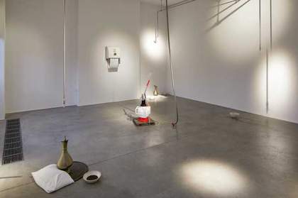 A white room and grey floor with a few objects on the floor and a hand towel on the wall.