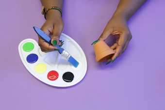 Photograph of two hands painting a plant pot