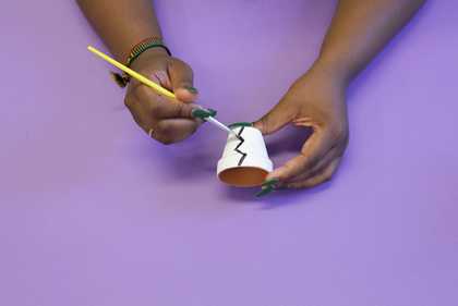 Photograph of two hands painting a plant pot