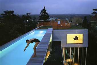 Office for Metropolitan Architecture Villa DallAva 1991 Colour photograph of a woman diving in to a pool and a man standing on grass on the rooftop of a contemporary house