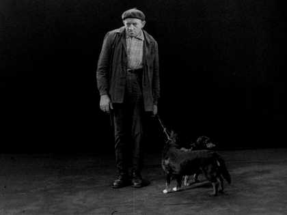 Black and white film still of "Hamburg" where two men and a woman stand next to a ladder and drop written signs.