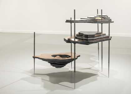 A freestanding sculpture made of layers of metal that resembles a land mass