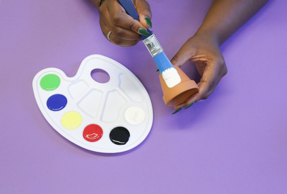 Photograph of two hands painting a plant pot