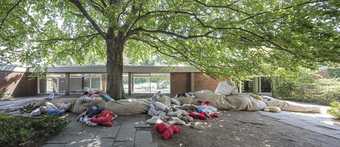 Landscape photograph of the installation 'Collective Conscience' showing a series stuffed cloth torsos in the courtyard of a mid-century building