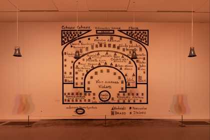 Installation by Oswaldo Macio showing 4 silver bells hanging from the ceiling. Behind is a mural of black text and lines painted directly on the gallery wall.