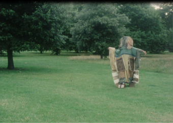 Film still of a person covered in fabrics walking on a lawn
