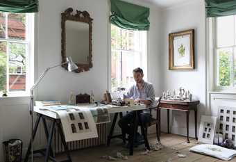 The artist Pablo Bronstein sitting at a table at his home