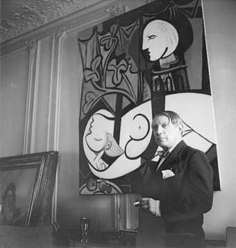 Pablo Picasso with his painting Nude, Green Leaves and Bust 1932 at rue La Boetie, Paris. Photographed by Cecil Beaton, 1933