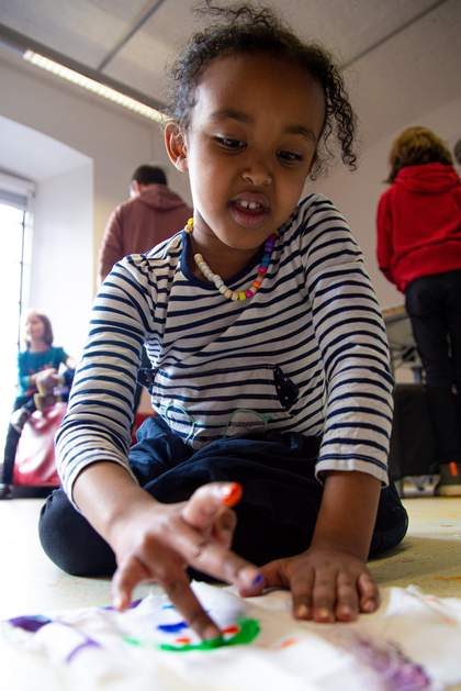 A small child sits on the floor as they paint using their fingers