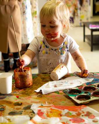 A toddler holds a paintbrush in their hand about to paint a piece of paper