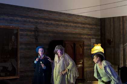 Three characters interact with each other in a living room theatre set