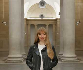 Photograph of Susan Philipsz standing in front of the installation with the speakers behind her